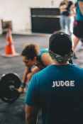 man in blue crew neck shirt staring at woman trying to lift barbell